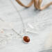  A playful 18" sterling silver necklace with a 10mm Baltic amber oval pendant on a light wood table, surrounded by soft decor. 
